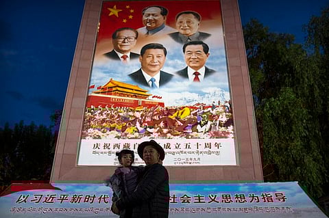 In this June 1, 2021 photo, a man holding a child pose for a photo in front of a large mural depicting Chinese President Xi Jinping and other Chinese leaders at a public square at the base of the Potala Palace in Lhasa in western China's Tibet Autonomous Region. (Mark Schiefelbein/AP)