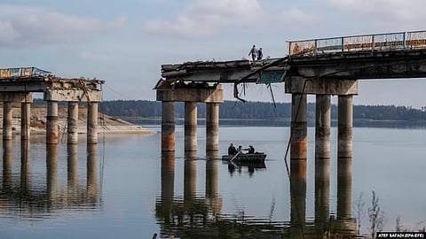 Civilians cross the Siverskiy Donets River by boat under a damaged bridge in the liberated city of Stariy Saltiv east of Kharkiv. It's estimated that Ukraine will need hundreds of billions of dollars over the next 10 years to rebuild its devastated economy and infrastructure.