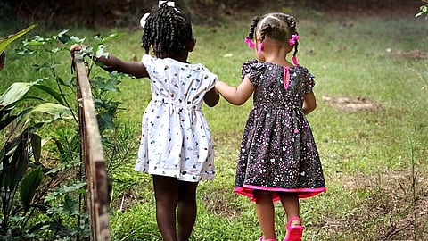 Two young girls standing outdoors, looking at plants together in a grassy area