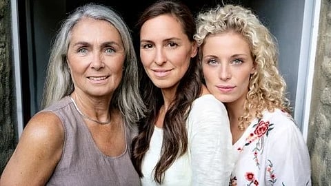 A portrait of three women from different generations standing close together and smiling at the camera