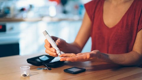 A person in a red top using a glucose testing device, holding a small pen-like tool near their hand