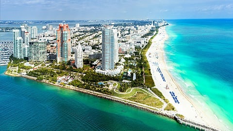 Aerial view of a coastal city with tall buildings, a long beach, and turquoise water.