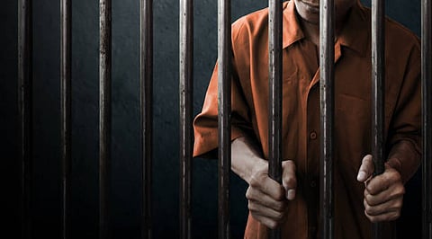 Person in an orange outfit holding prison bars.