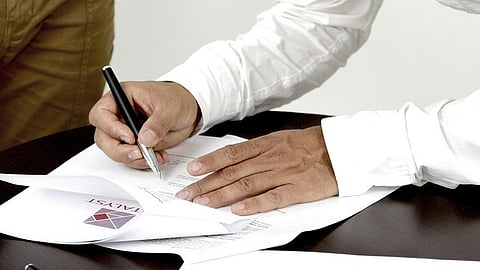 Person signing a document with a pen while holding the paper