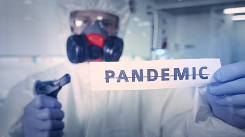 Person in protective suit and mask holding a paper with the word “PANDEMIC.”