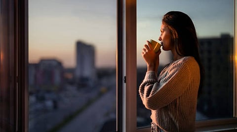 A woman gazes out a window, admiring the vibrant colors of a sunset.