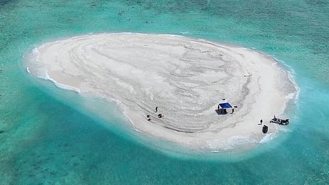 A white sand island with several people enjoying the beach under a clear blue sky.