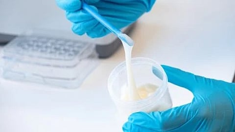 A person wearing blue gloves holds a cup with a spoon, preparing to serve or taste a beverage.