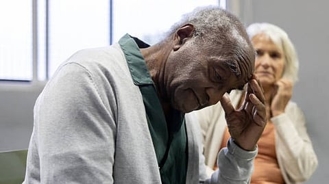 An elderly person sitting with a hand on their face, looking thoughtful.