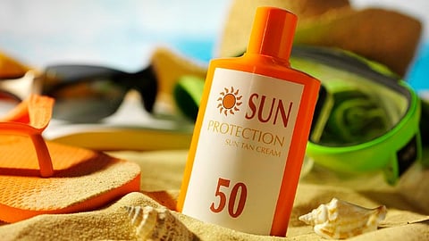 SPF 50 sunscreen bottle placed on a beach towel with sunglasses in the background.