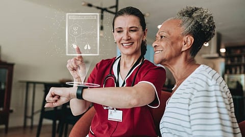 A woman points to a screen while discussing information with a nurse in a healthcare setting.
