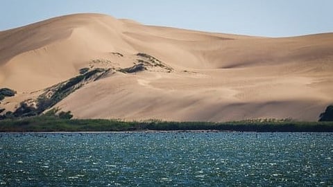 A desert landscape featuring a boat in the background against a clear blue sky.