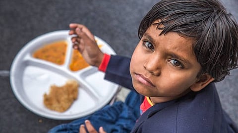 A young child is seated at a table, eating food from a plate with a joyful expression on their face