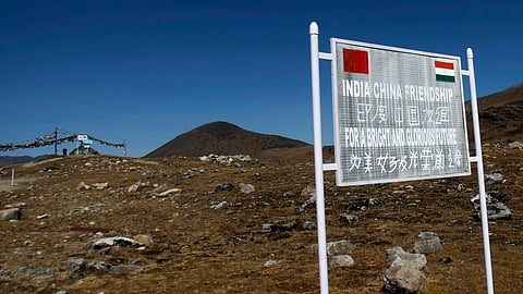 Signboard marking the India-China border with flags and mountains in the background.