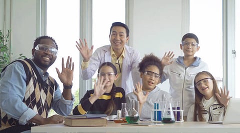 Students and teacher in a science lab smiling and waving.