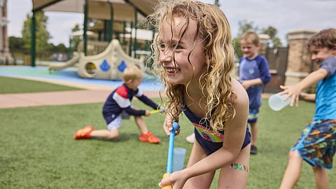 Smiling children playing with water outdoors on a playground.