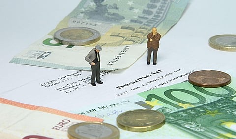 Miniature figures standing on euro banknotes and coins, symbolizing finance or economy.