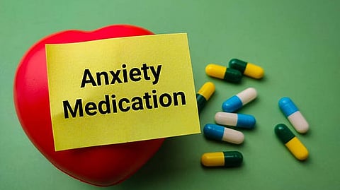 Pills beside a note labeled “Anxiety Medication” on a green surface.