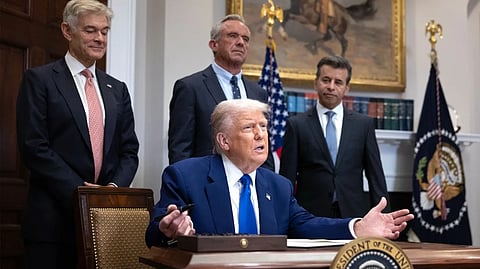 A man speaking at a desk with others standing behind him in an office.