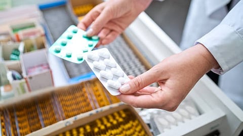 A person holding two packs of tablets in a pharmacy.