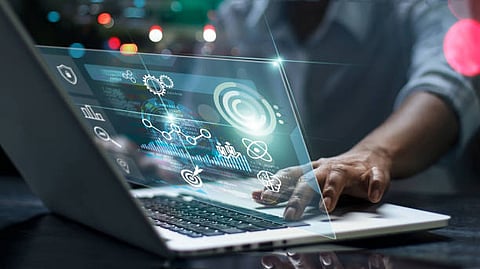 A person using a laptop with digital data graphics projected above the screen.