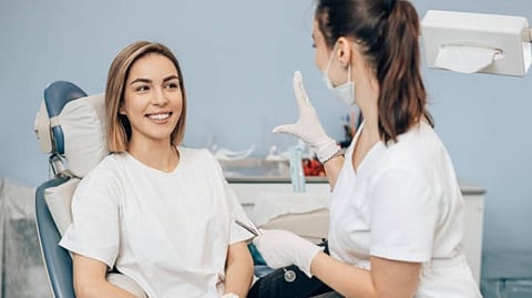 woman sitting in a dental chair smiling while a dentist talks to her.