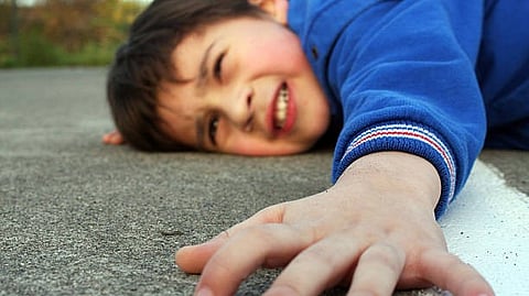 The image shows a young boy reaching out and holding onto a wall with a strained expression.