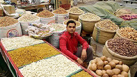 he image shows a man sitting in a market surrounded by large sacks of dry fruits and grains.