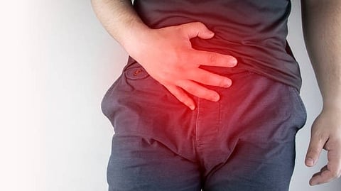 A person wearing a dark shirt is lying on their side, placing a hand on their lower back, with a red highlight indicating pain or discomfort in that area.