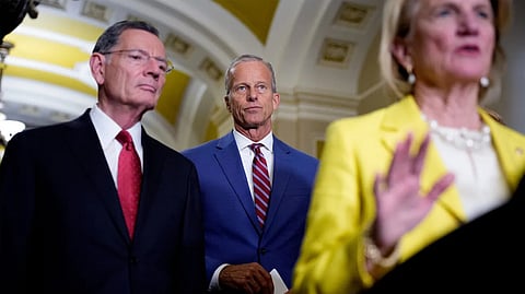 Three formally dressed people standing indoors, appearing to speak or attend an official event.
