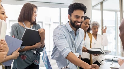 Group of people smiling and discussing documents together in an office setting.