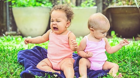 children sitting in the park, one is crying amd one is sitting