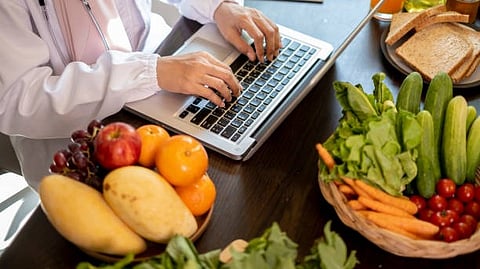 Person working on laptop with fresh fruits and vegetables on the tables.