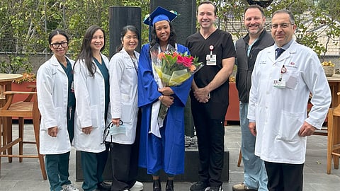 Group photo of graduates in blue gowns and people in white lab coats, with one person holding a banquet of flower