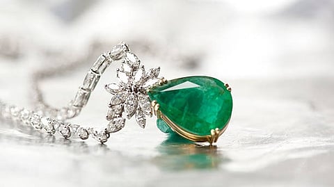 close up of a diamond necklace with a large green emerald pendant.