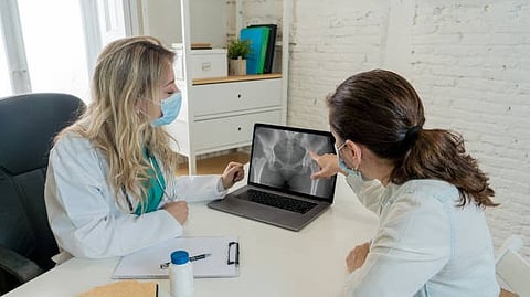 Two doctors wearing white coats and face masks are examing an x-ray image on a laptop in a medical office.