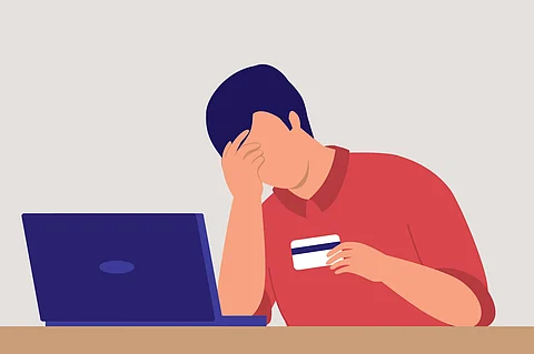 The image shows a person sitting with a hand on their head, staring at a card and laptop in visible tension.