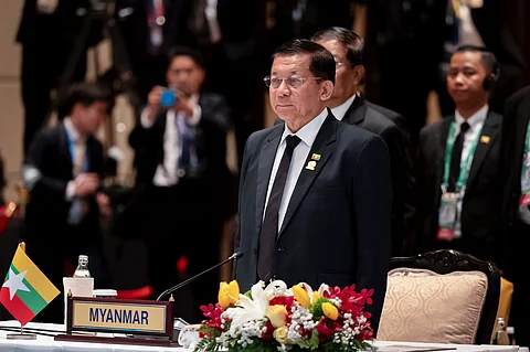 The image showcase Myanmar's military leader in a press conference or a meet he is wearing formals and addressing some people. many other are standing behind him wearing formals
