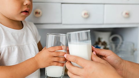 Infant holding glass of milk.