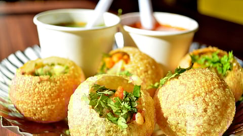 A plate of pani puri garnished with coriander leaves and chutney.