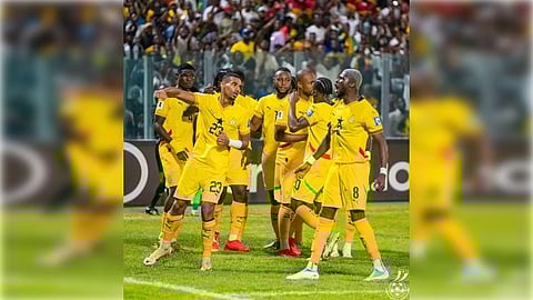 A group of soccer players in bright yellow uniforms celebrate on a grassy field. One player gestures energetically as a lively crowd watches, conveying joy and excitement.