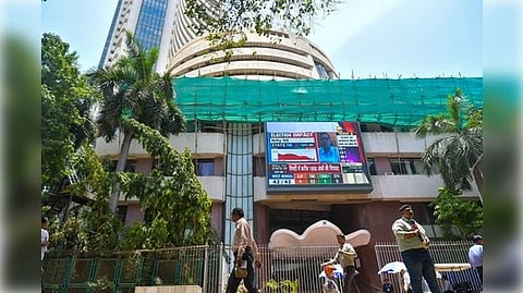 Street view of the Bombay Stock Exchange building with a digital display, people walking by, surrounded by tall palm trees under a clear blue sky.