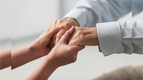 Two hands are gently holding an elderly person's hands, conveying warmth and support. The focus is on the hands, creating an intimate and caring tone.