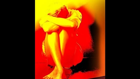 A person sits curled up with arms wrapped around knees against a vivid yellow and red background, conveying emotions of solitude and introspection.