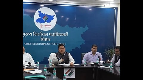 Meeting at Chief Electoral Office, Bihar with officials seated at a table, microphones, and water bottles. A map and logo are on a blue backdrop.