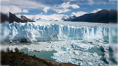 Expansive glacier with towering icy cliffs, floating ice chunks in turquoise water, surrounded by rugged mountains under a partly cloudy sky. Majestic and serene.