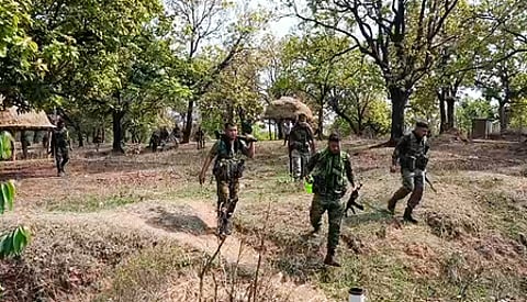 A group of indian soldiers in uniforms walk through a dense forest with green foliage. They appear vigilant and focused, moving in a strategic formation.