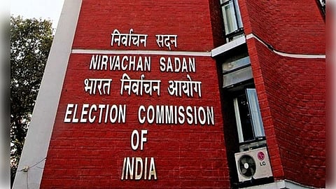 Red brick building with signage reading "Election Commission of India" in Hindi and English. An air conditioning unit is visible. The mood is official.