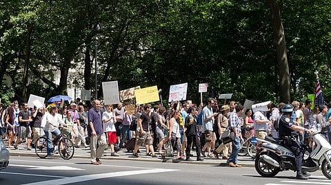 People protesting by holding banners with slogans on the streets of America. Some are walking, some are in the bicycle and motorcycle.