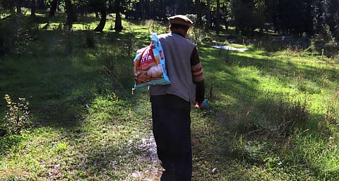 Muhammad Sadiq standing in a field with a sack slung over his shoulder.